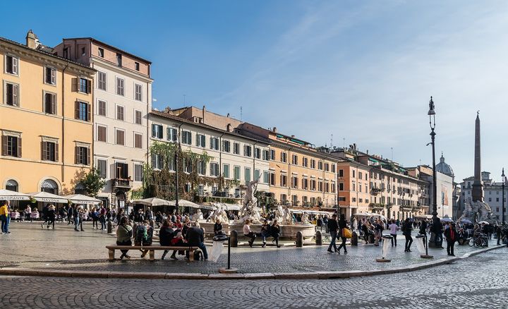 Piazza Navona on a sunny day, with ochre and pink houses, a fountain and the obelisk at the far end.