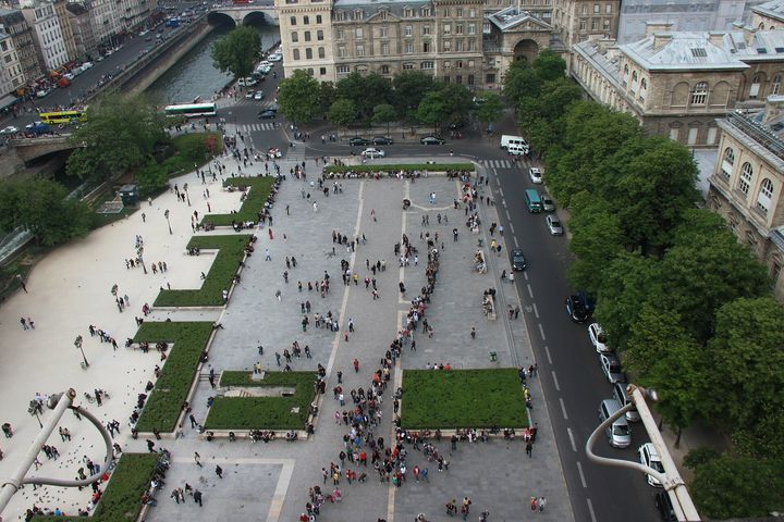 The square in front of Notre-Dame seen from above, with a long line of visitors and the Seine behind.